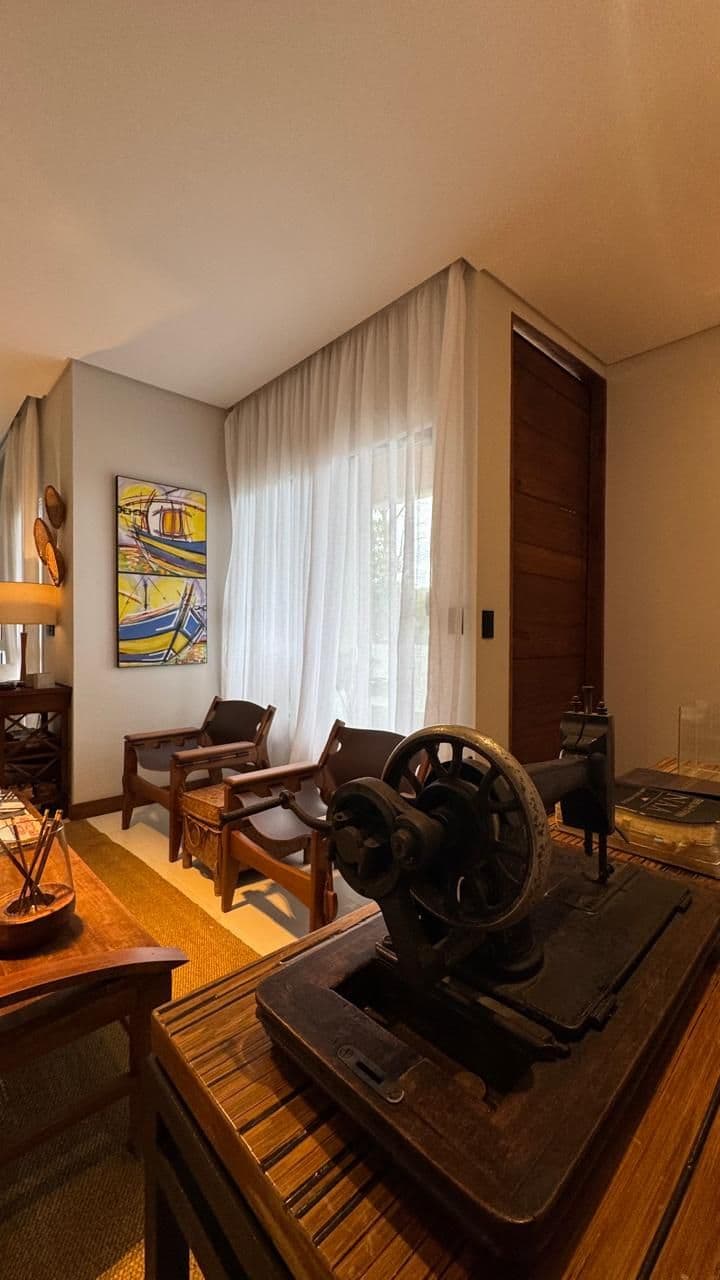 Sala com poltronas de couro e madeira, mesa de madeira e quadro colorido.