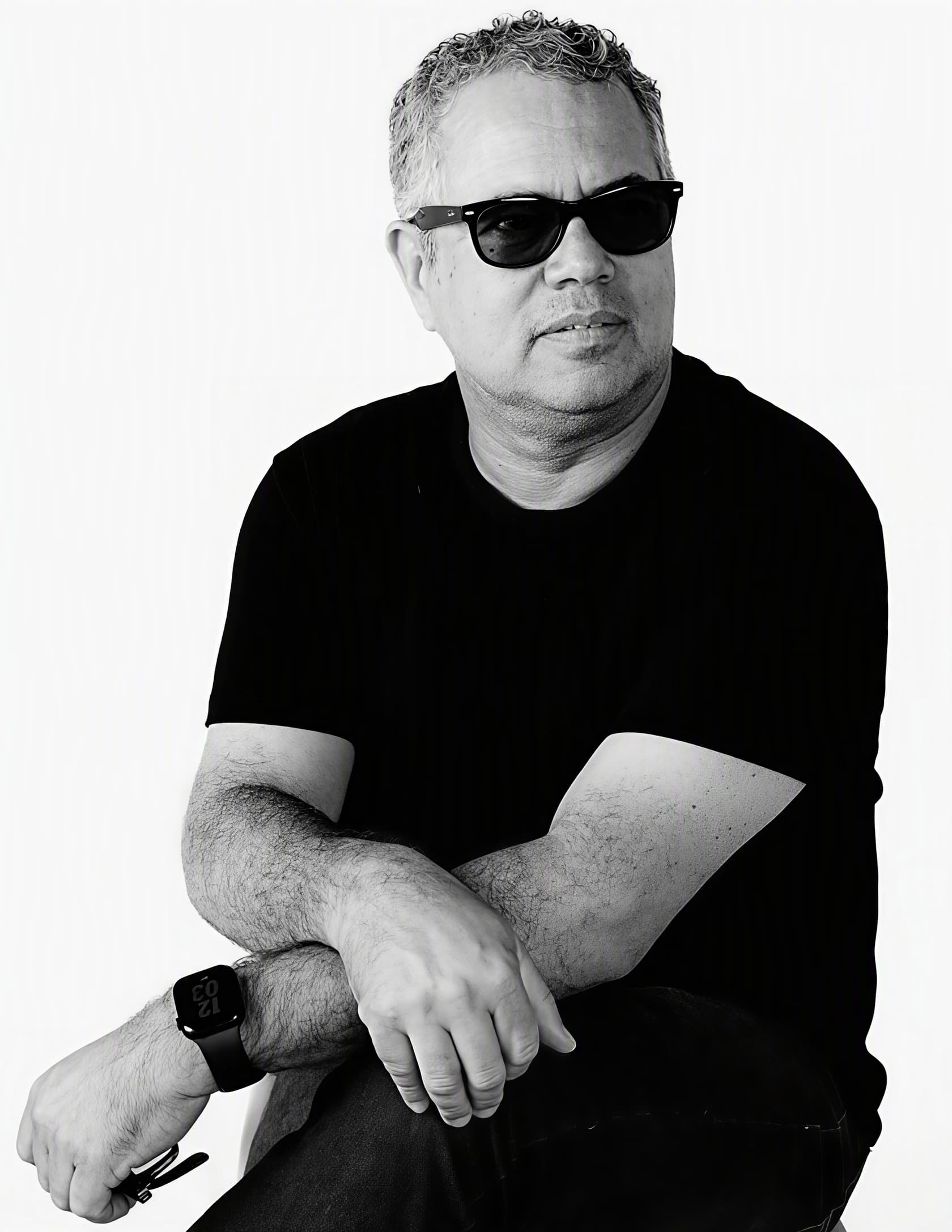 Retrato em preto e branco de Ricardo Almeida, sentado, de óculos escuros.